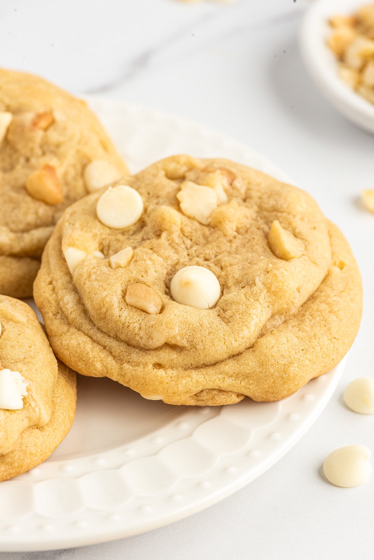 A close-up shot of a cookie with white chocolate chips and macadamia nuts.