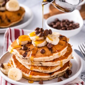 Syrup being poured over a stack of banana chocolate chip pancakes