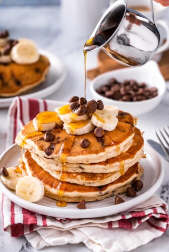 Syrup being poured over a stack of banana chocolate chip pancakes