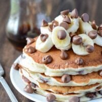Stack of Banana Chocolate Chip Pancakes on a white plate topped with bananas and chocolate chips.