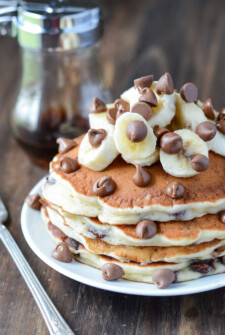 A stack of Banana Chocolate Chip Pancakes topped with fresh bananas and chocolate chips.