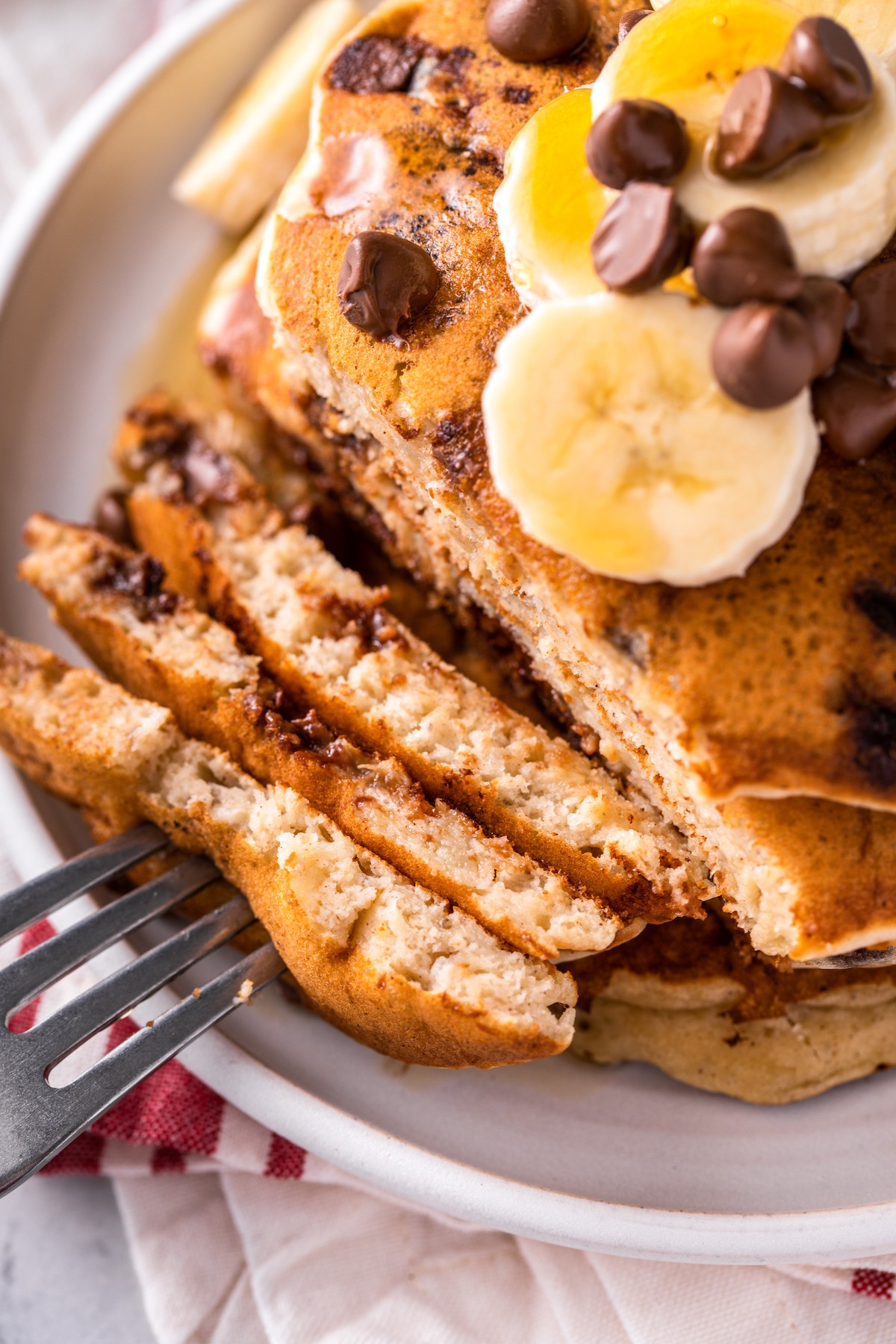 A fork holding pieces of chocolate chip pancakes next to a stack of pancakecs