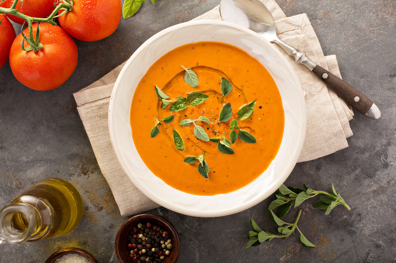 creamy tomato soup in a bowl with tomatoes and pantry staples