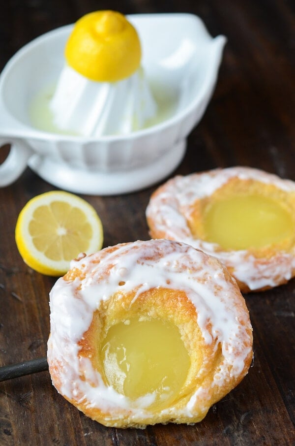 A Lemon Being Juiced with a Juicer Behind Two Freshly Made Lemon Danishes