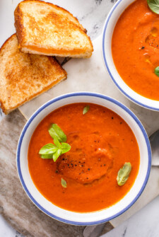 Two bowls of tomato soup with herbs, and two halves of a grilled cheese sandwich.