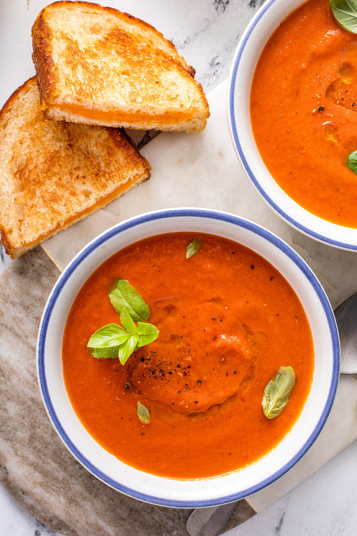 Two bowls of tomato soup with herbs, and two halves of a grilled cheese sandwich.