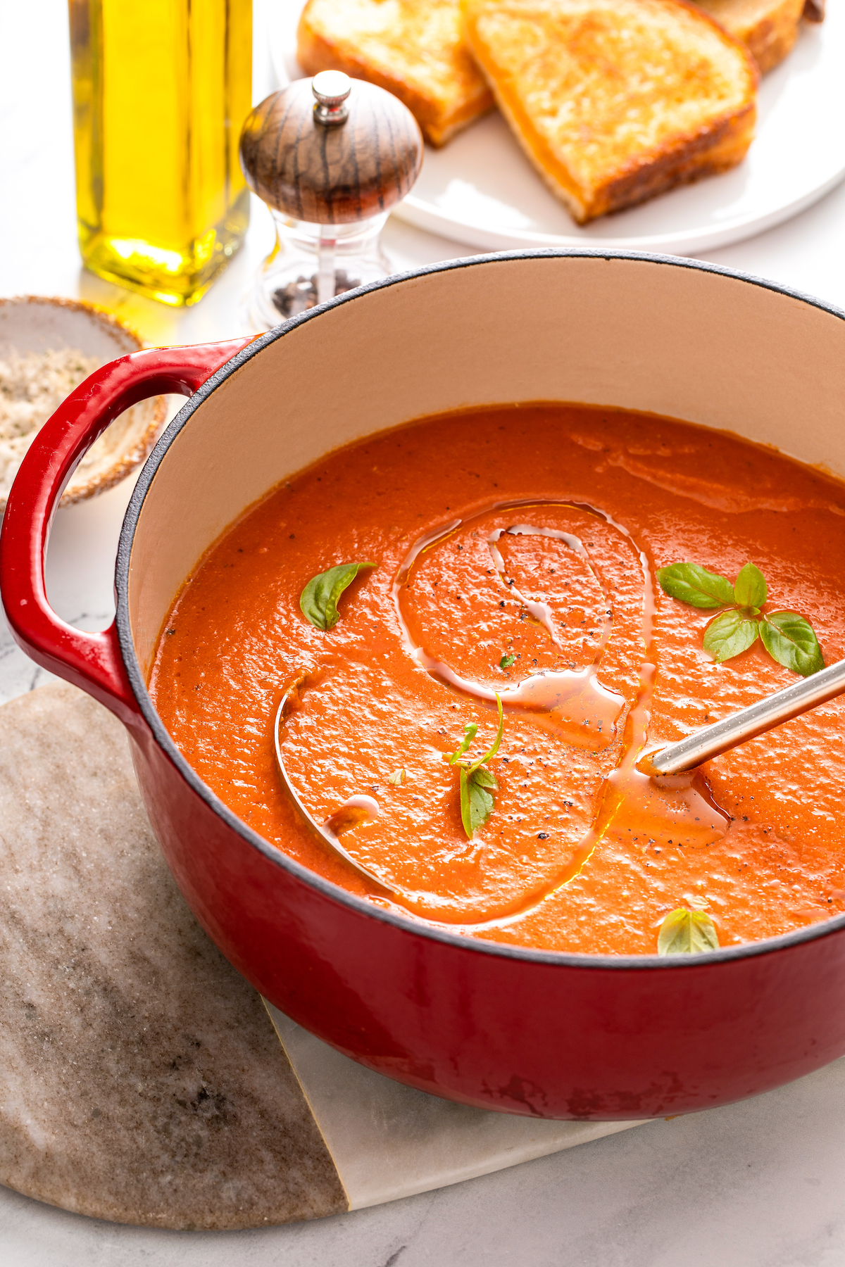 A red Dutch oven with tomato soup and a ladle.