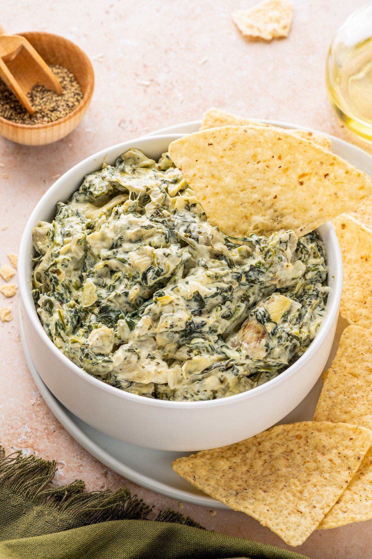 A white bowl of spinach artichoke dip with a tortilla chip in it.