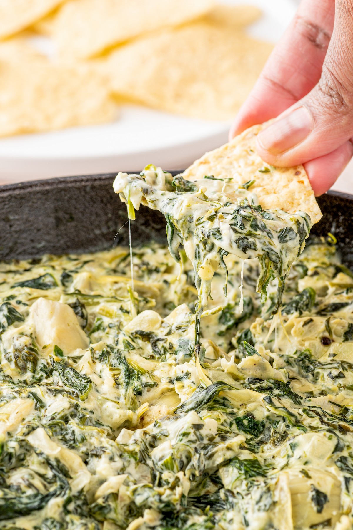 Dipping a tortilla chip into homemade spinach artichoke dip.