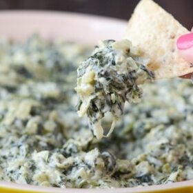 Stovetop Spinach and Artichoke Dip in a yellow dish, chip being dipped.