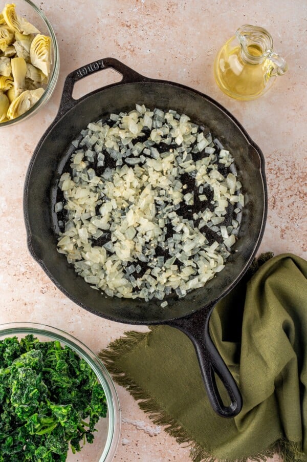 A cast-iron skillet with onions and garlic cooking in it.