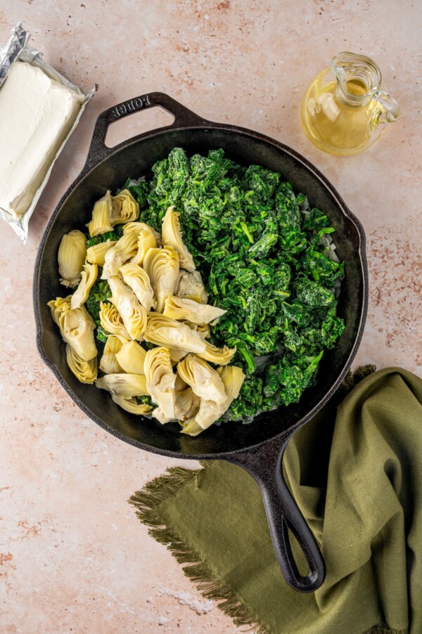 Adding spinach and artichokes to a skillet.