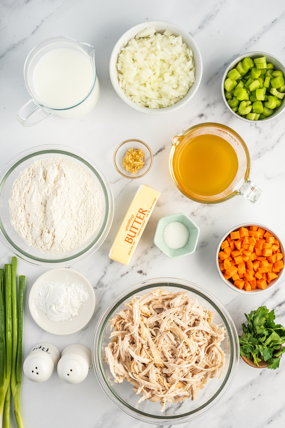From top left: Milk, diced onion, celery, flour, garlic, chicken stock, butter, salt, carrots, baking powder, shredded chicken, chopped parsley, green onions, salt, and pepper.