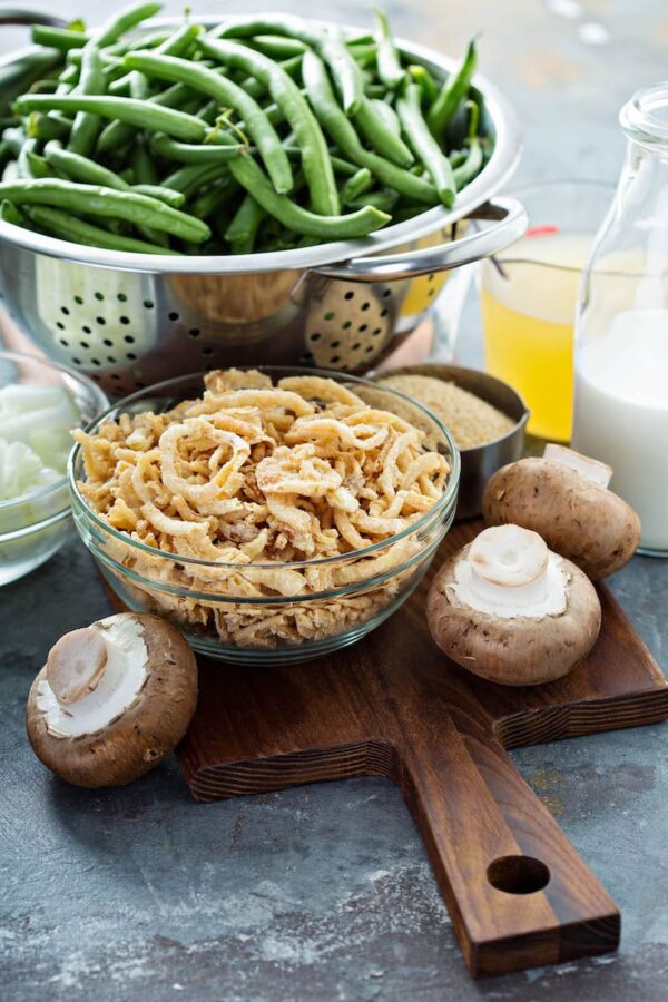 Green beans in a bowl next to fried onions, mushrooms and chopped onions.
