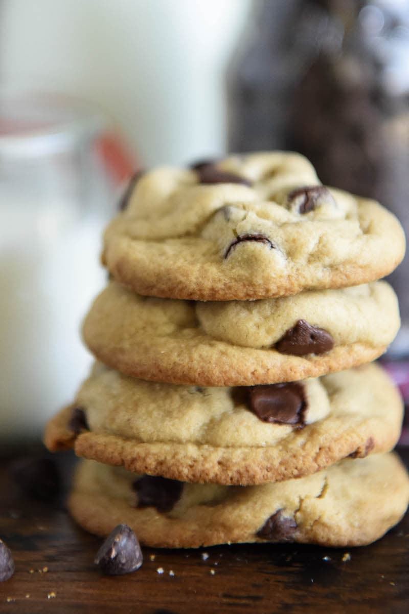 A stack of classic chocolate chip cookies with milk in the background.