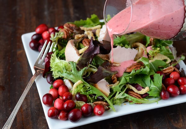 Cranberry vinaigrette is poured over turkey salad on a plate next to a fork.