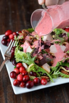 Cranberry vinaigrette is poured over turkey salad on a plate next to a fork.