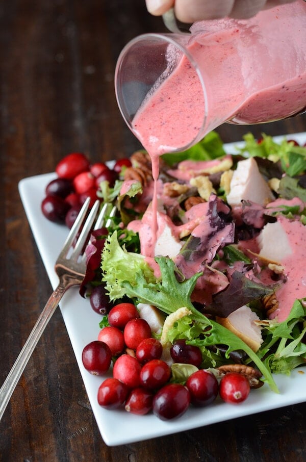 Cranberry vinaigrette is poured over turkey salad on a plate next to a fork.