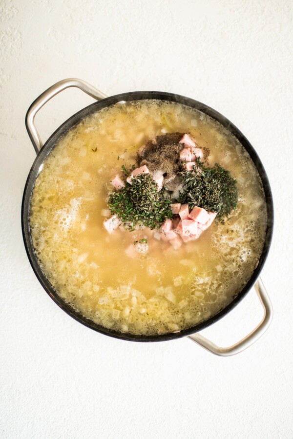 Ham pieces, herbs, and beans cooking in a broth.