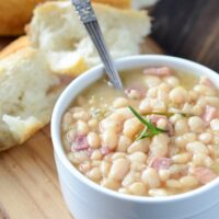 Rosemary Ham Bean Soup in a white bowl with a spoon and bread