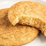 Two snickerdoodle cookies on a plate, one with a bite missing