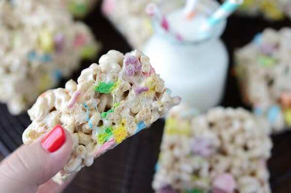 A Hand Holding a Lucky Charm Marshmallow Treat Over a Platter Displaying More Cereal Bars