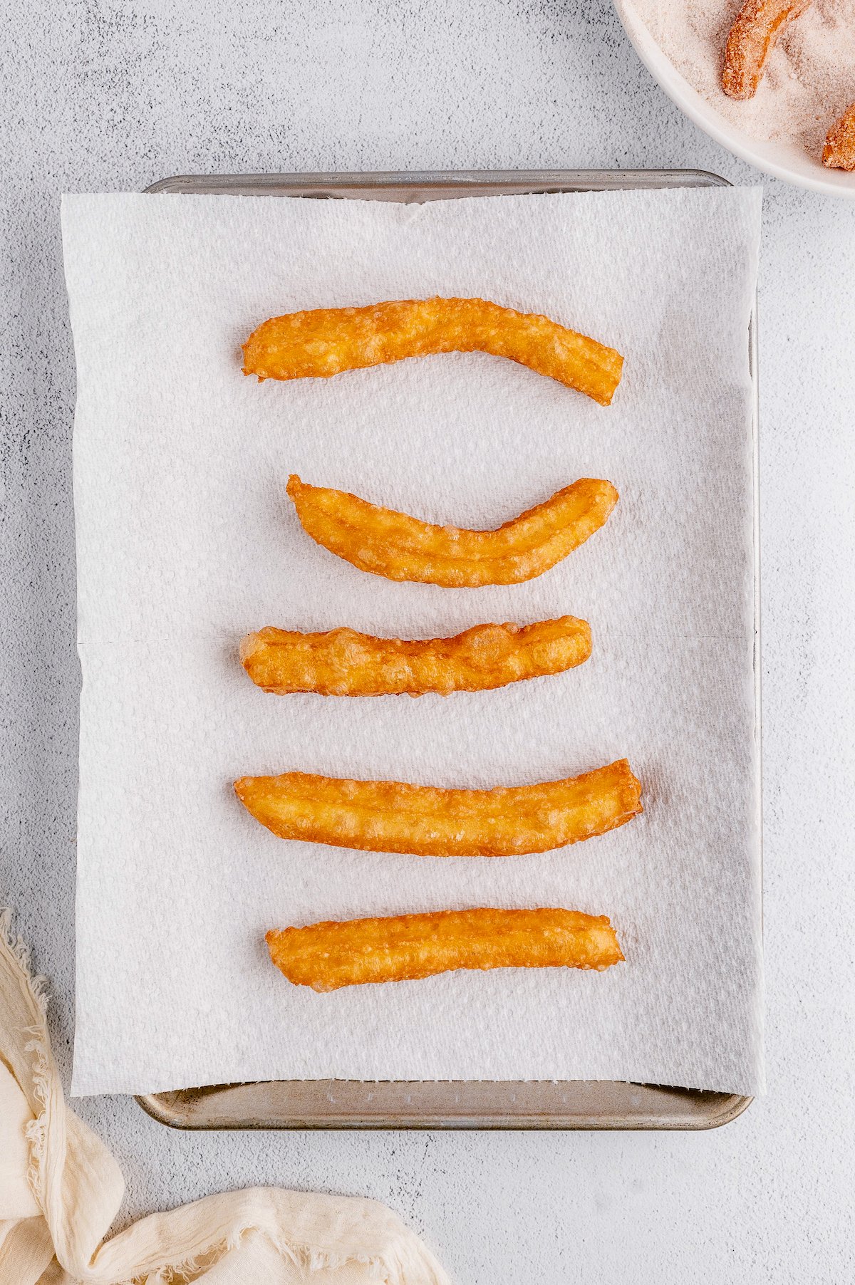 Fried churros on a paper towel-lined tray.