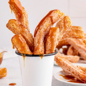 Homemade churros in a serving cup drizzled with caramel sauce.
