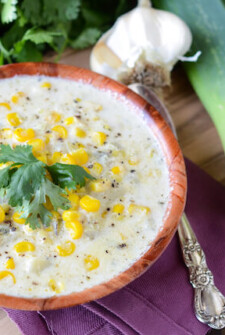 Creamy Sweet Corn and Roasted Poblano Soup in a wooden bowl with a spoon, garlic, and leeks