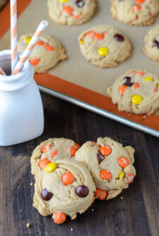 Three Reese's Pieces Peanut Butter Cookies piled in front of a baking sheet with more cookies on it