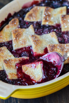 Berry Cobbler in a yellow baking dish with a spoon scooping cobbler out