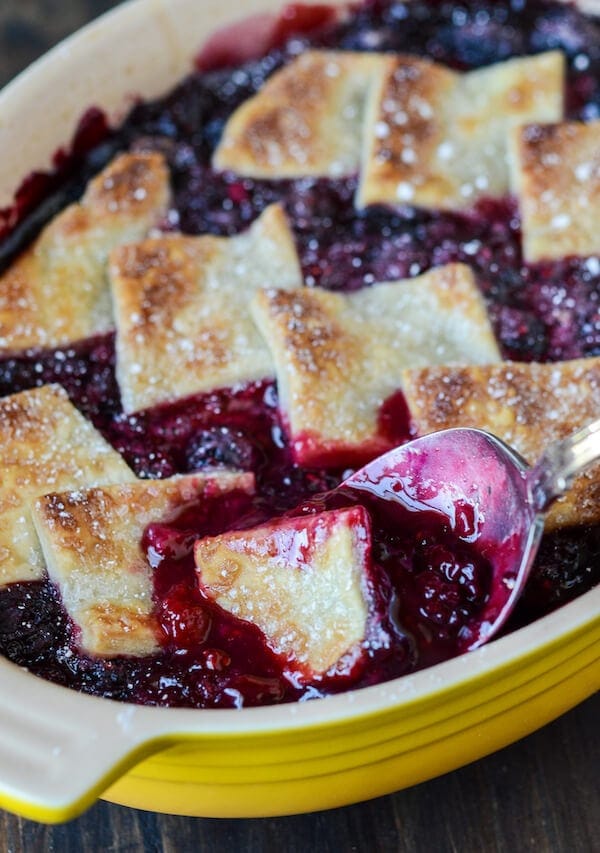 Berry Cobbler in a yellow baking dish with a spoon scooping cobbler out