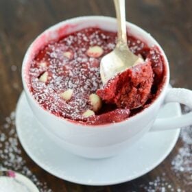 Red Velvet mug cake in a white coffee mug and a spoon on a wooden surface