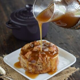 Donut Bread Pudding on a white plate with a spoon and Rum Sauce being poured over it