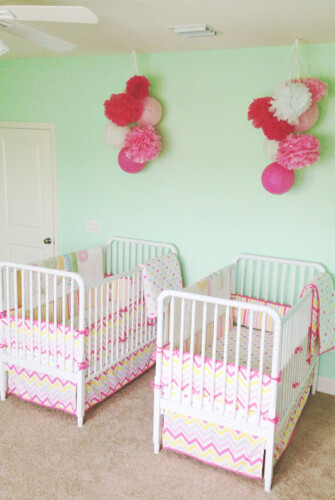 A Nursery for Twin Girls with Light Green Walls and Pink Cribs