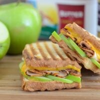 Apple, Cheddar & Turkey Panini on wooden board with apples in the background