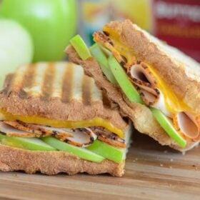 Apple, Cheddar & Turkey Panini on wooden board with apples in the background