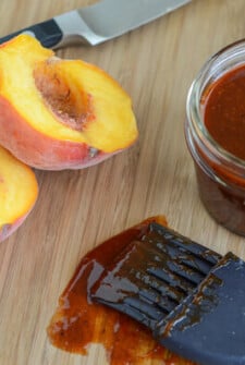 Peach BBQ Sauce in a glass jar with a halved peach on a wooden board