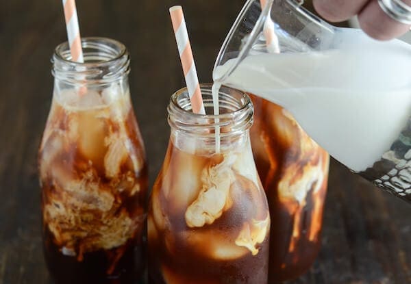 Thai Iced Tea with cream being poured in glass and pink and white straws