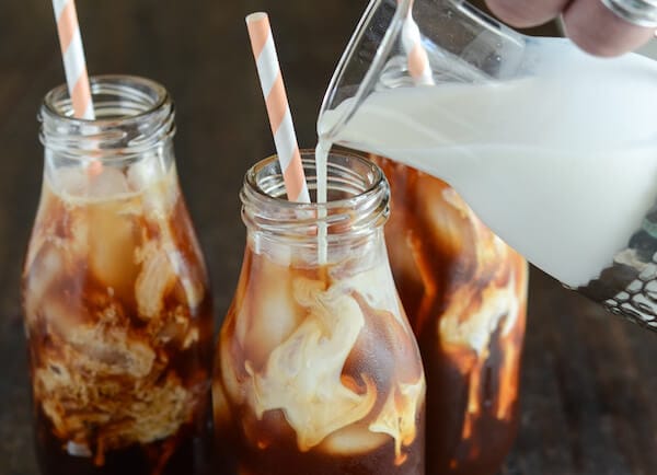 Thai Iced Tea with cream being poured in glass and pink and white straws