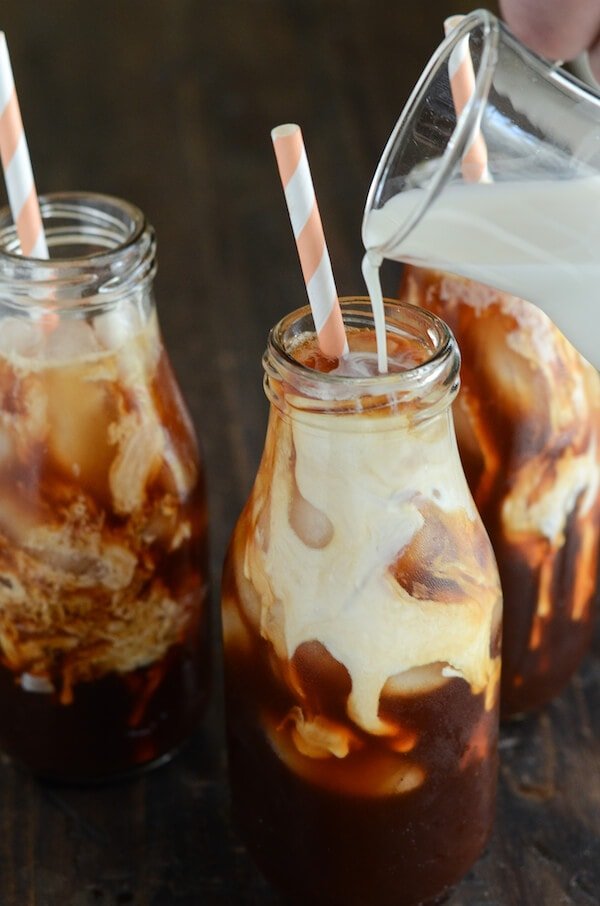 Thai Iced Tea with cream being poured in glass and pink and white straws