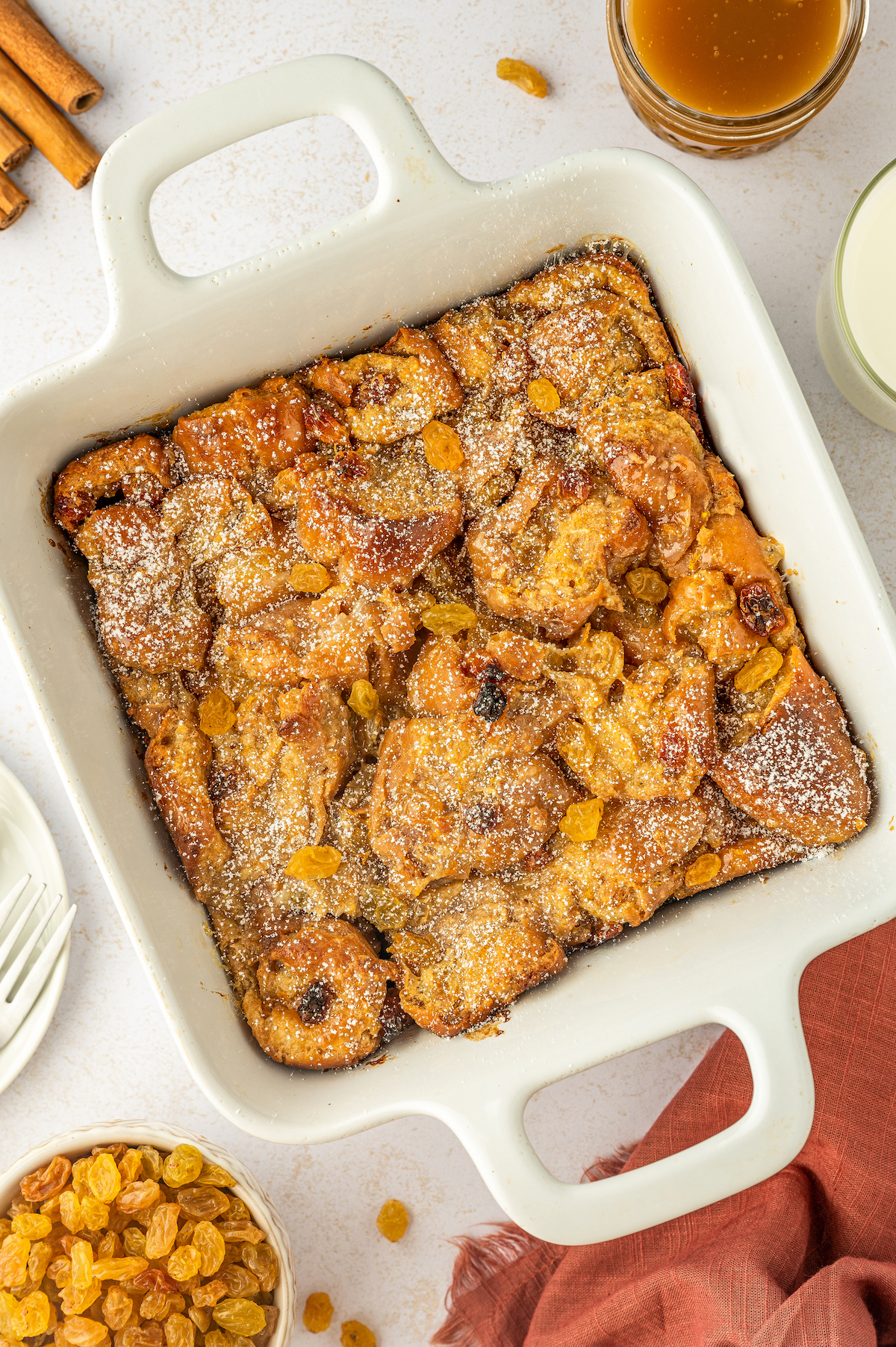 A baked pan of bread pudding made with donuts sprinkled with powdered sugar on top.