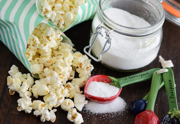 Sweet & Salty Kettle Corn in green and white bags with a jar of sugar and measuring spoons with sugar