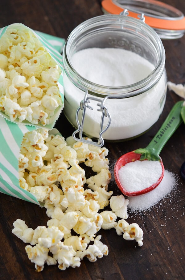 Sweet & Salty Kettle Corn in green and white bags with a jar of sugar and measuring spoons with sugar