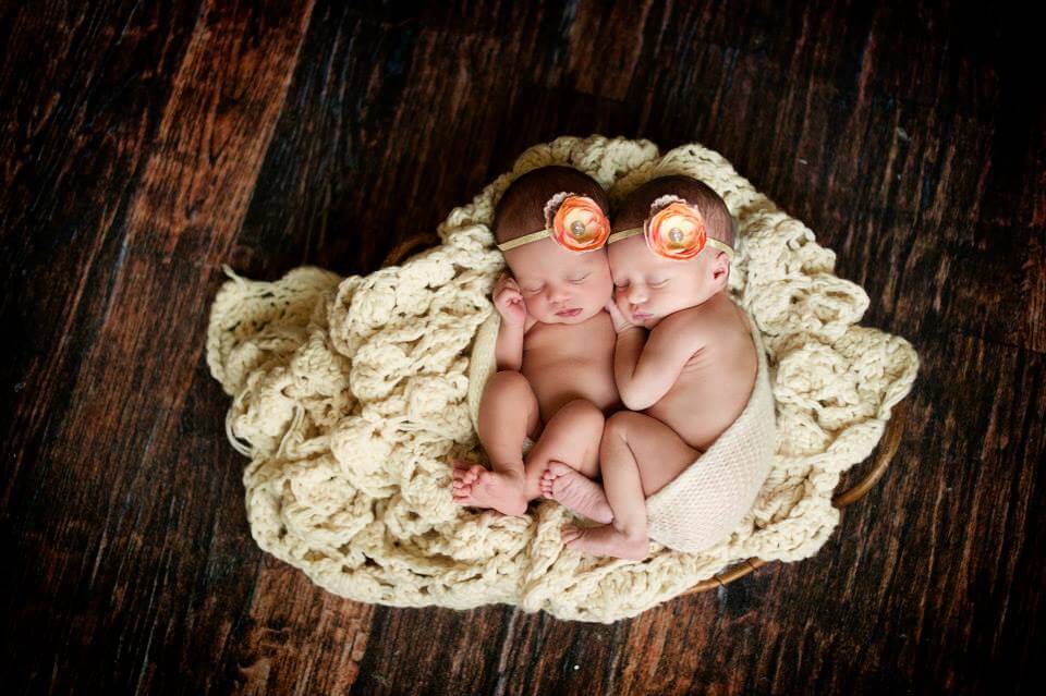 Two Baby Girls Sleeping on a White Knitted Blanket with Flower Headbands on their Heads