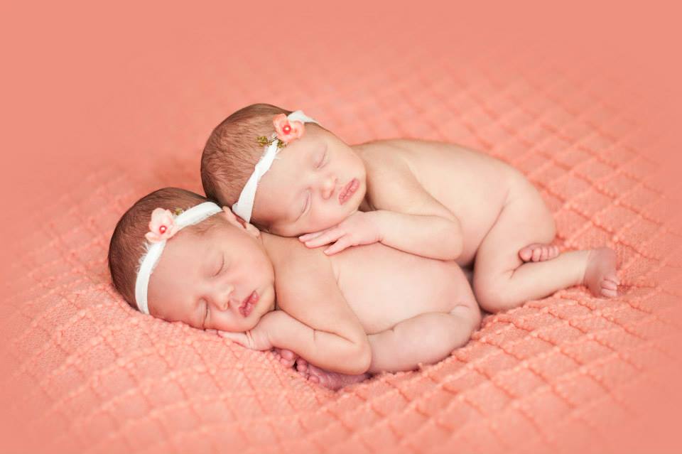 Two Twin Newborns Sleeping on Top of One Another on a Light Orange Blanket