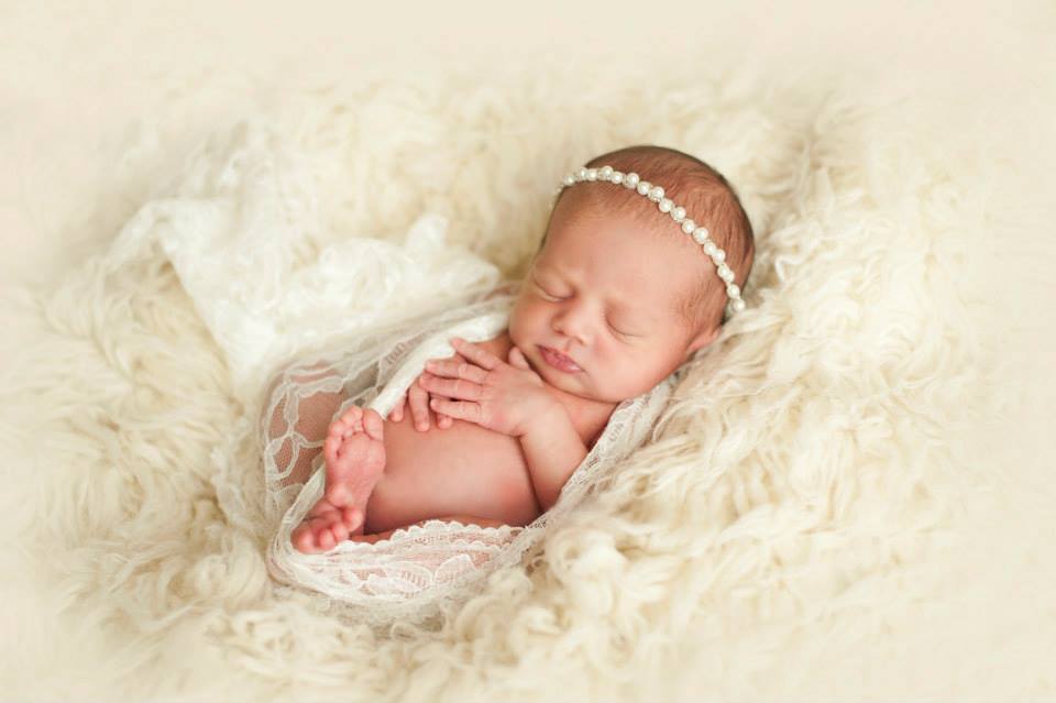 A Newborn Girl Wrapped Loosely in Lace and Sitting on a Fluffy Surface