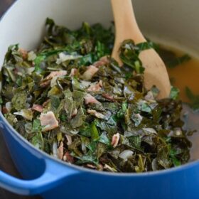 Beer Bacon Collard Greens in a blue pot with a wooden spoon