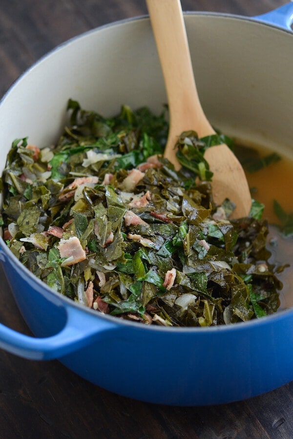Beer Bacon Collard Greens in a blue pot with a wood spoon