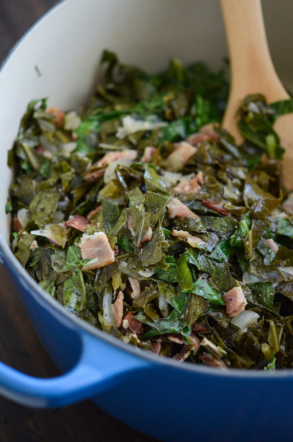 Collard Greens in a large blue pot with bacon and a wooden spoon